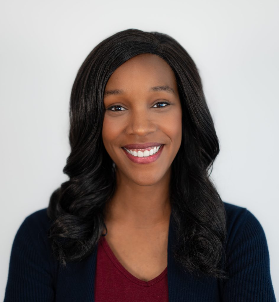 Smiling Black woman with wavy hair, wearing a burgundy top and navy cardigan.